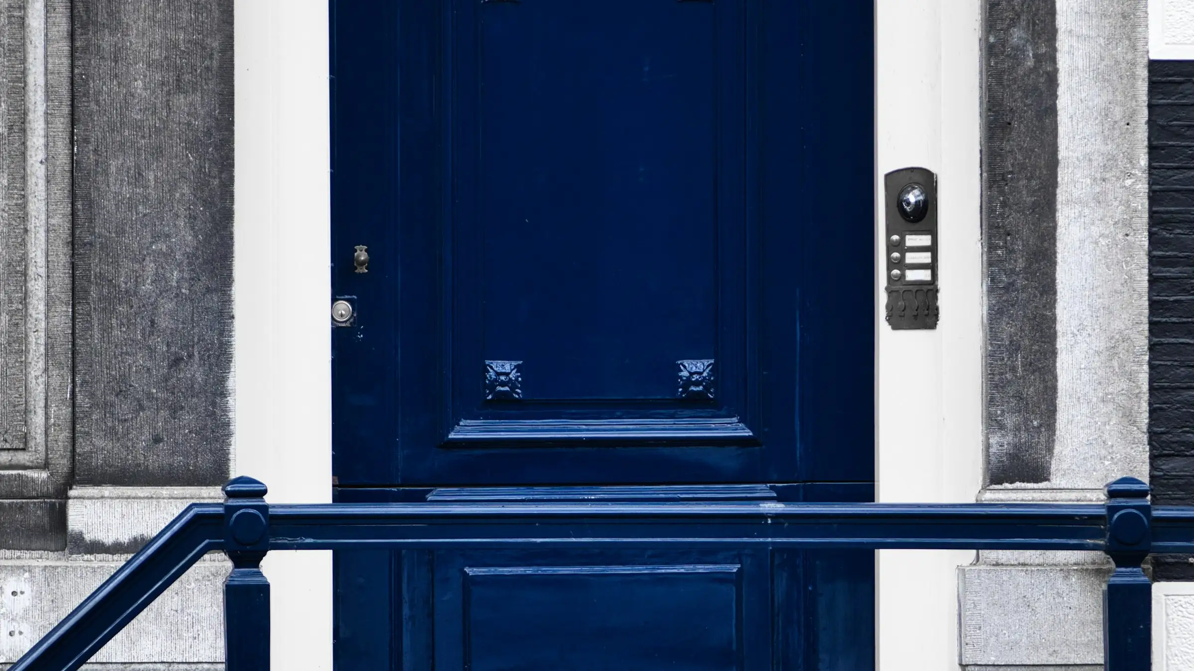 Donkerblauwe voordeur van een Amsterdams grachtenpand met een deurbelpaneel ernaast